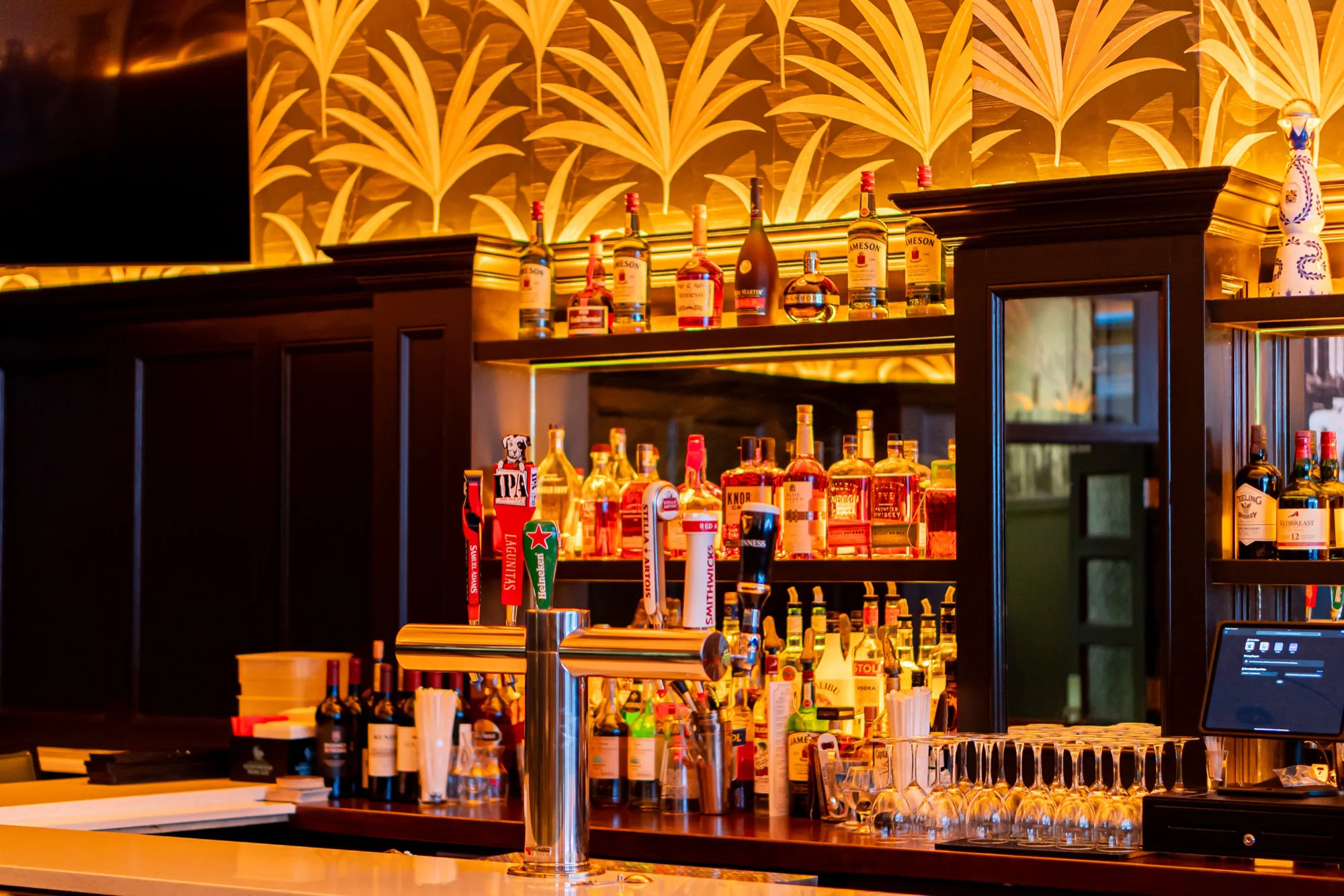 The Taft Bar: green leather stools along a dark timber bar, palm-leaf wallpaper lit gold