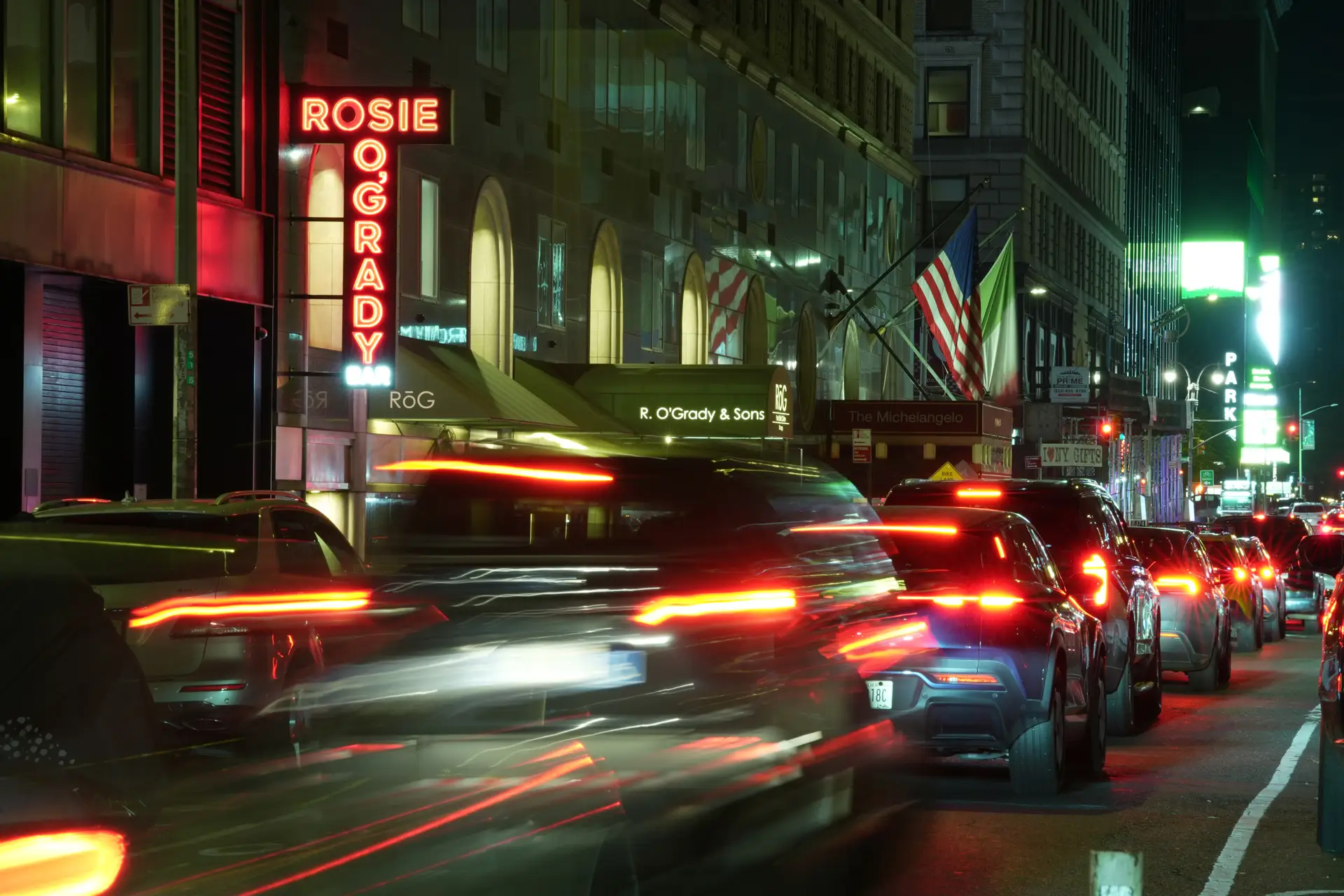 Rosie O'Grady's red neon sign on West 51st Street at night, traffic streaking past