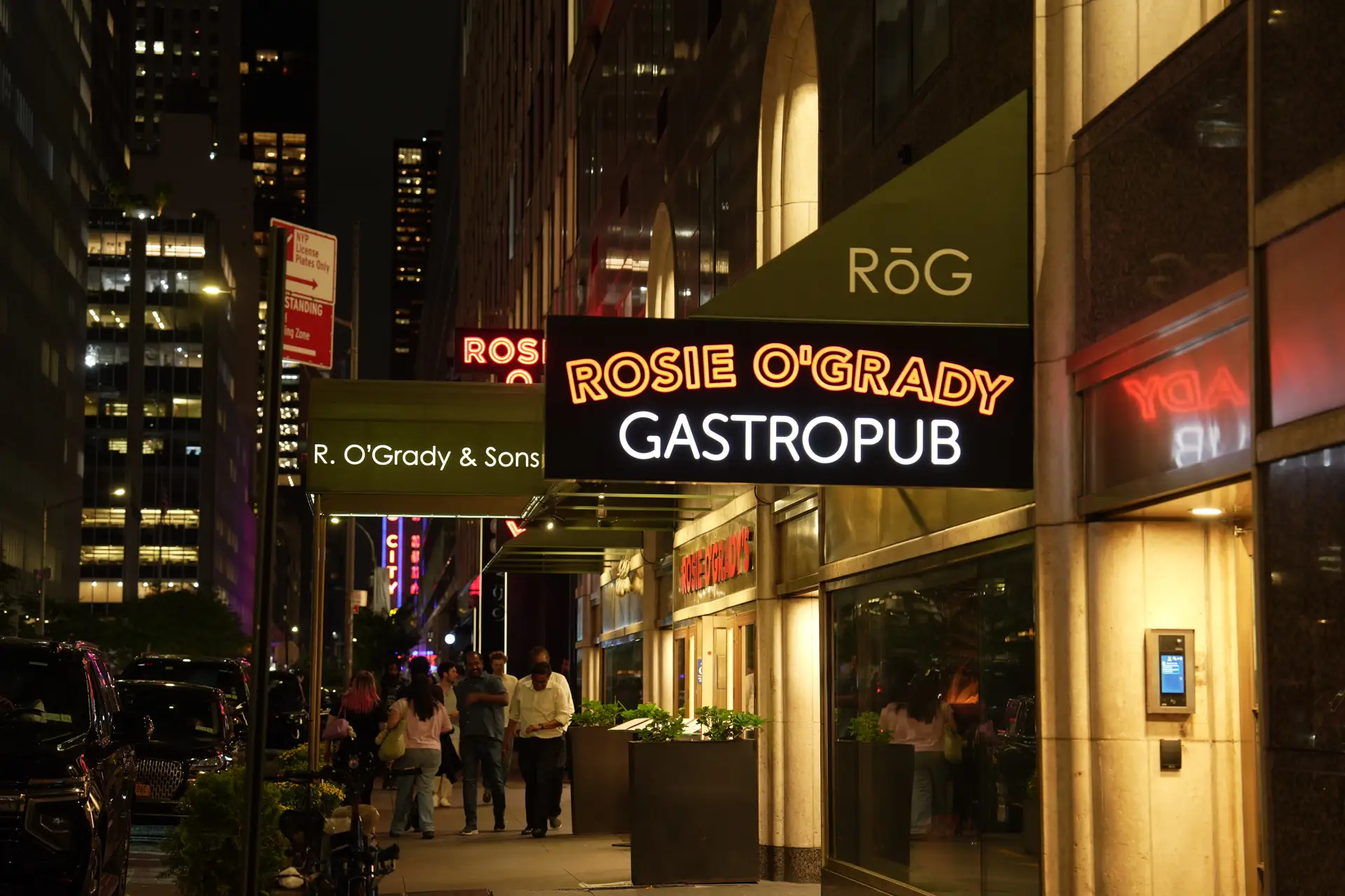 The lit Rosie O'Grady's and RÓG signs over the sidewalk on West 51st Street at night
