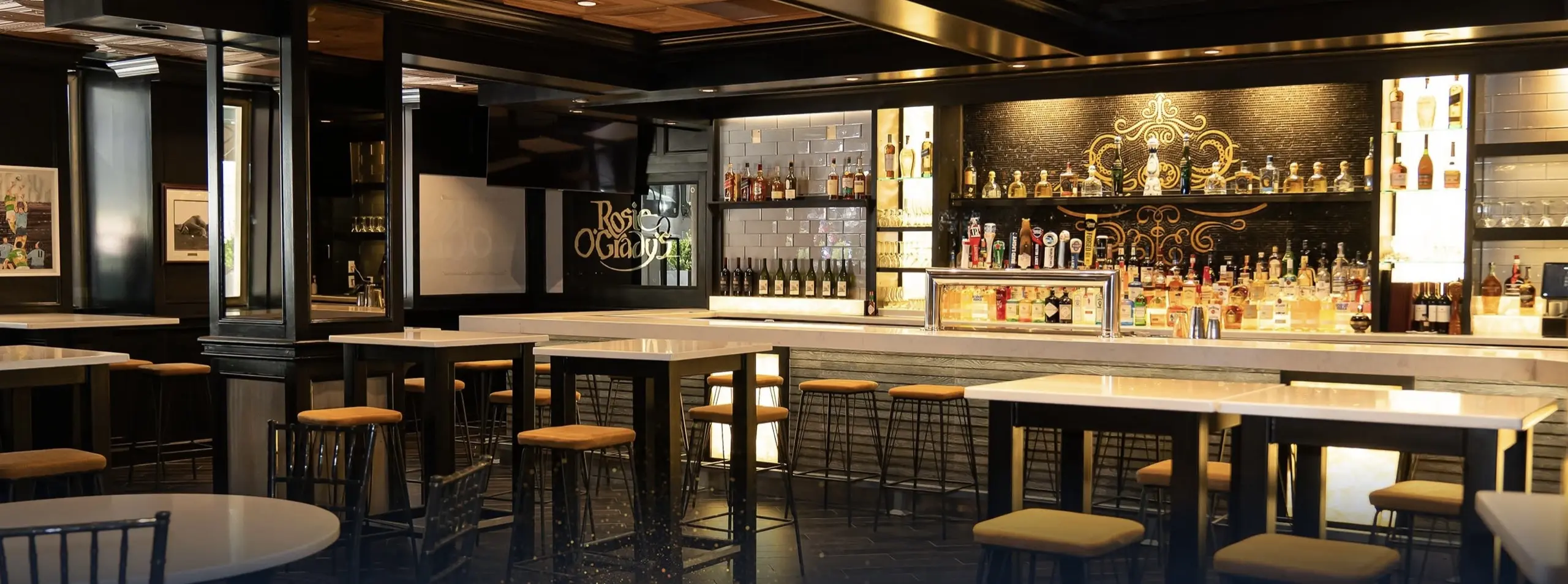 The main bar, the back bar lit and stools along the counter