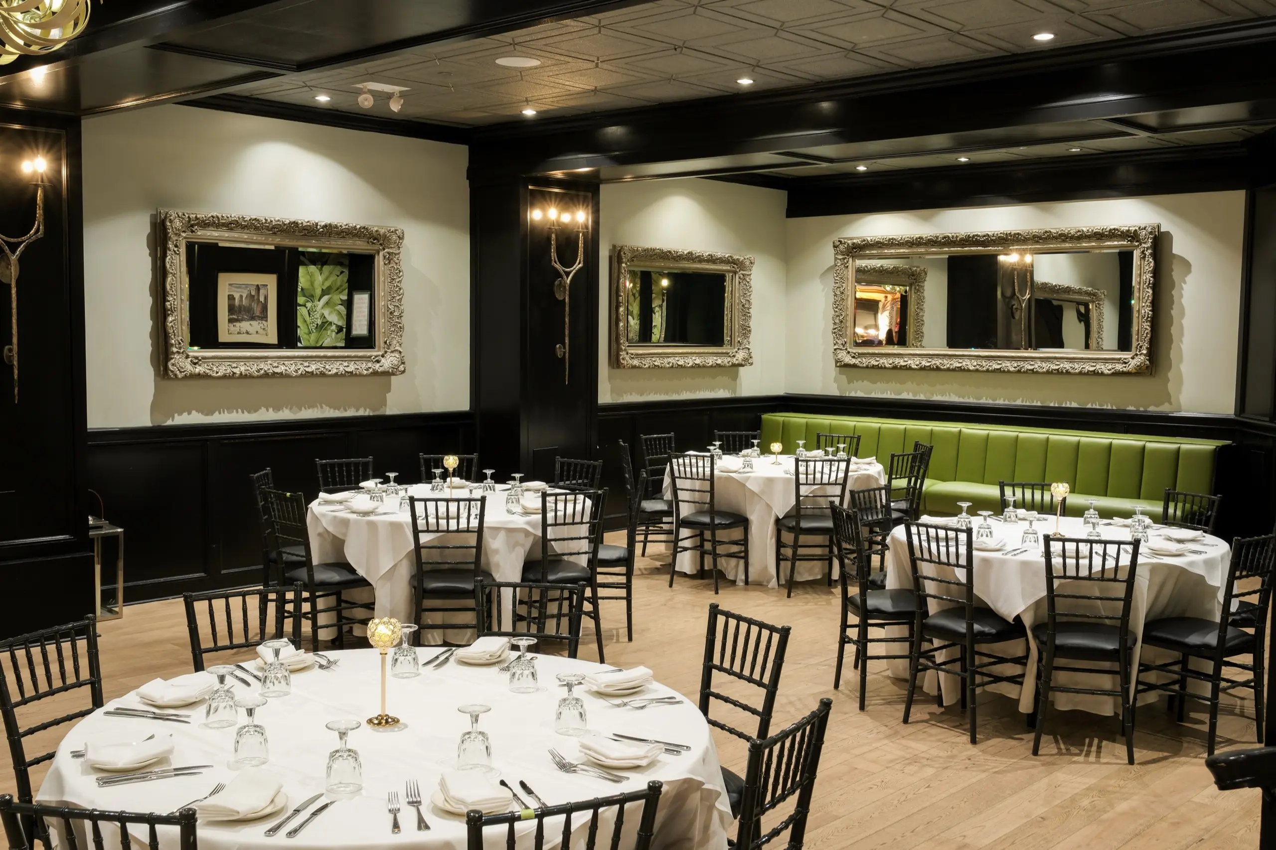 The main dining room set with round tables, green banquettes and gilt mirrors